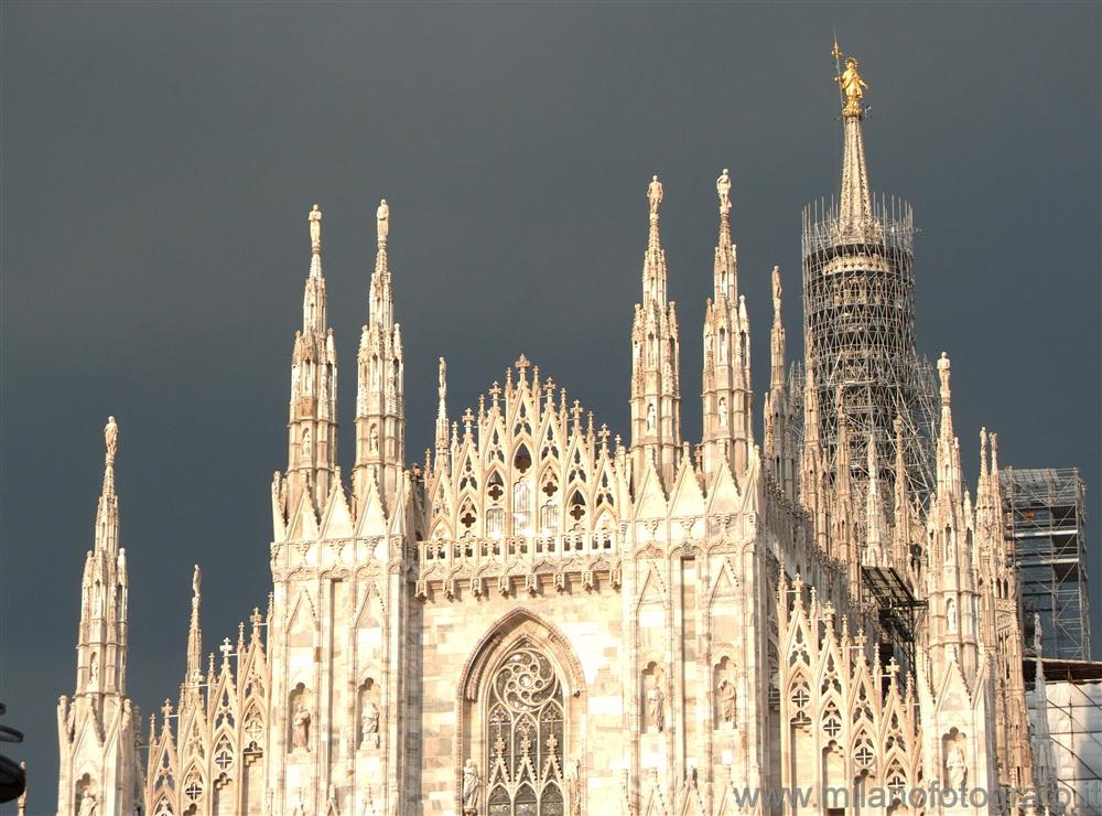 Milan (Italy) - The Duomo with dark clouds behind and illuminated by the sunset sun